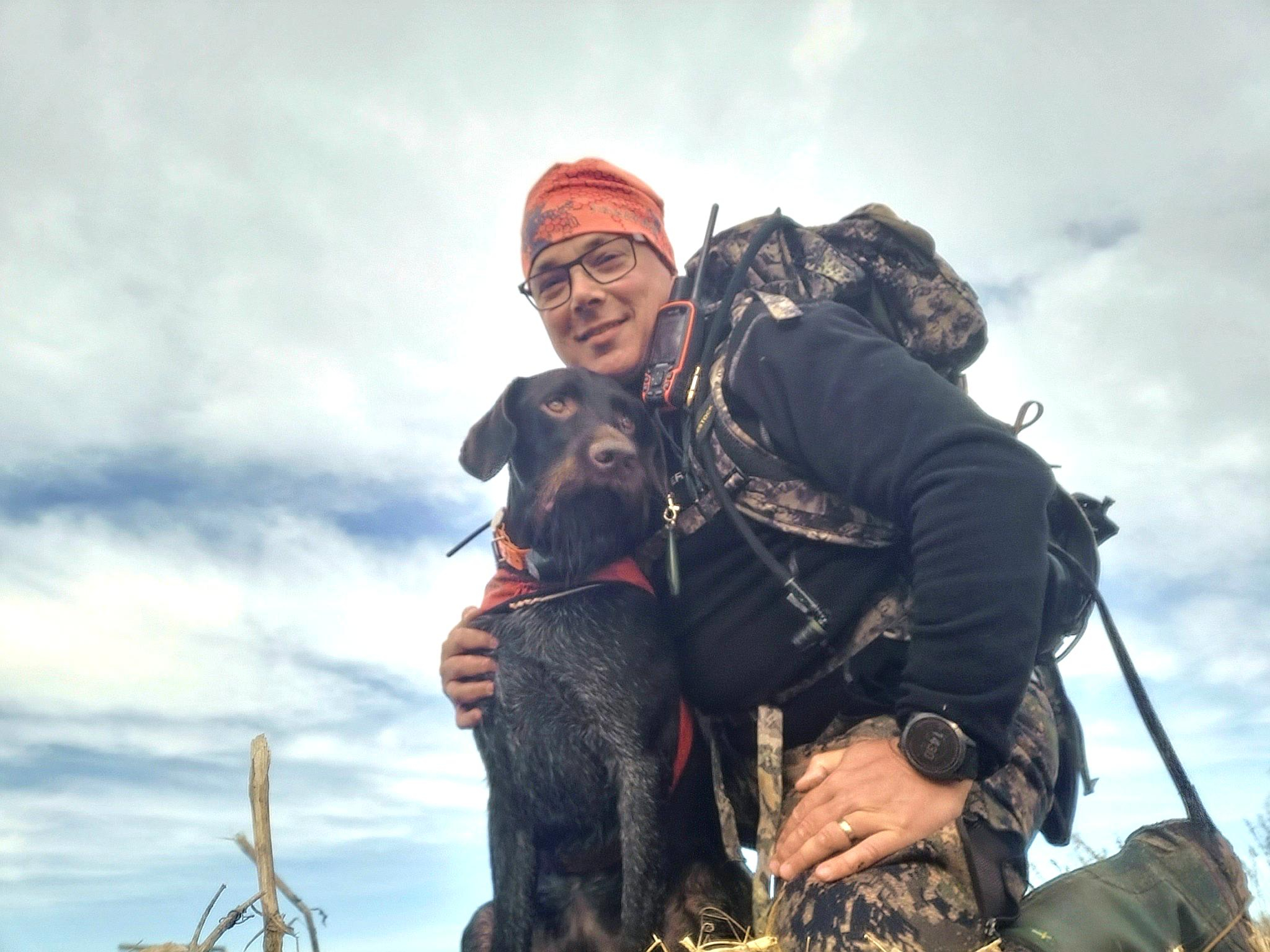 Mies ja koira pellolla metsästysreppu selässään